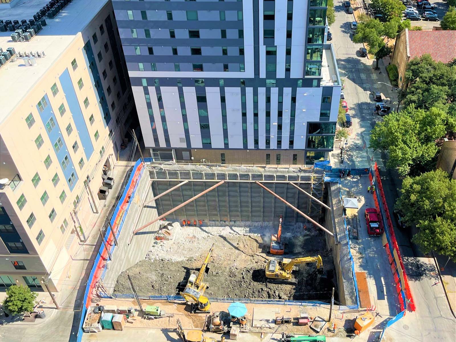 Deep urban excavation featuring an internal bracing system and soldier pile shoring installed by Oscar Orduno, Inc. to protect adjacent structures.