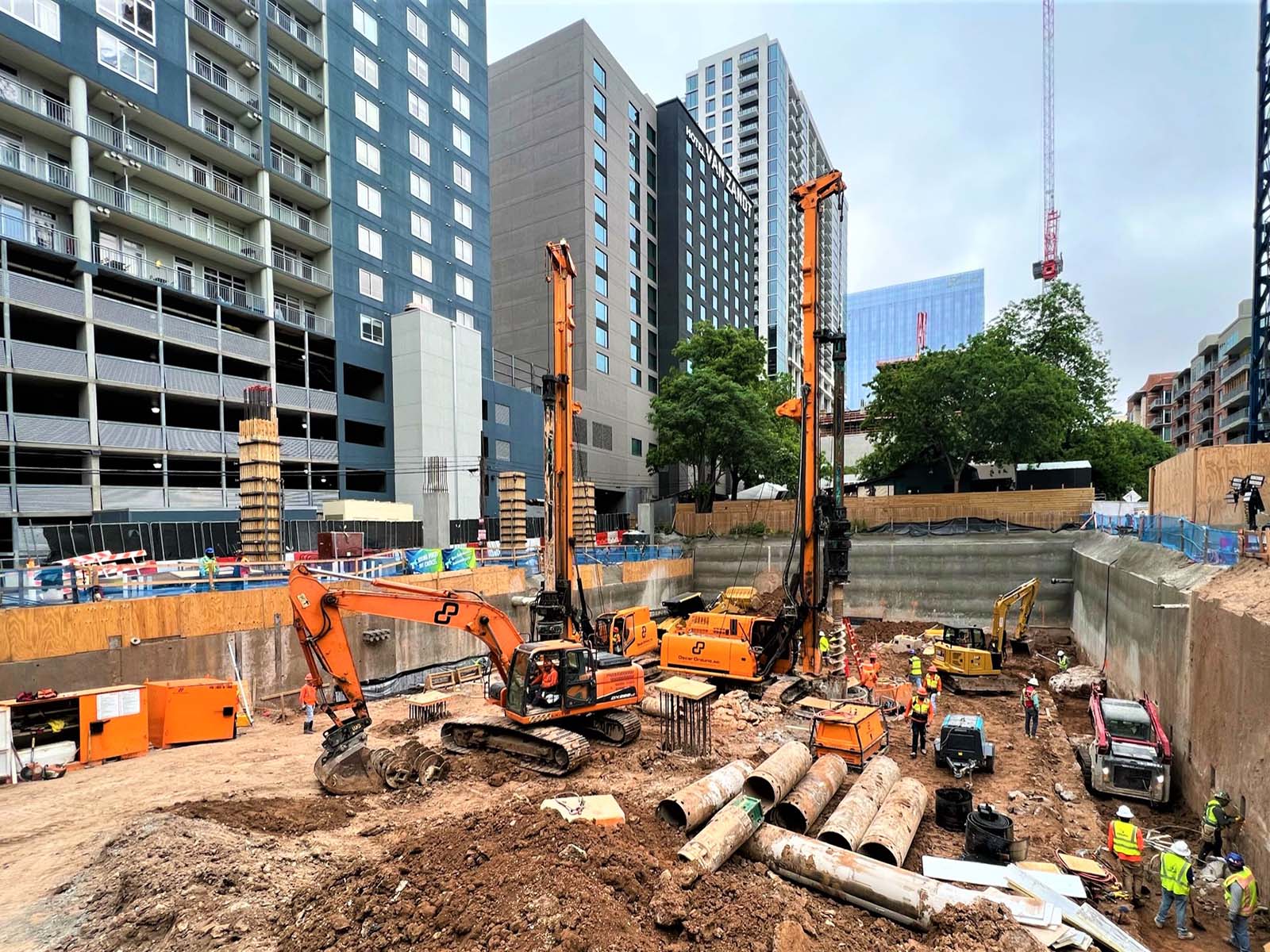 Dual drilling rigs and excavators from Oscar Orduno, Inc. installing Anchored Soldier Piles and Soil Nail Anchors at Paseo 80 Rainey in Austin, TX.