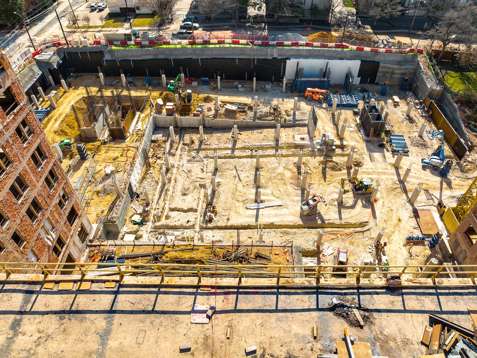 High-angle view of an organized urban excavation site featuring foundation columns and perimeter earth retention by Oscar Orduno, Inc.