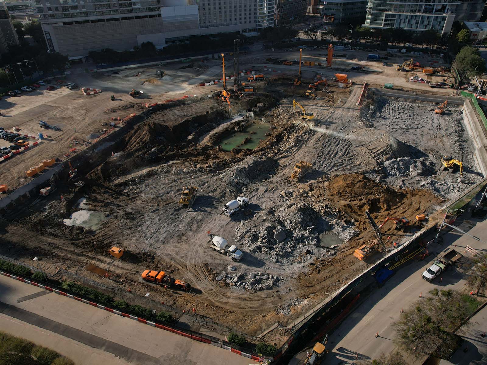 Aerial view of a major excavation site featuring Oscar Orduno, Inc. specialized drilling rigs and orange crawler excavators for deep foundation and earth retention.