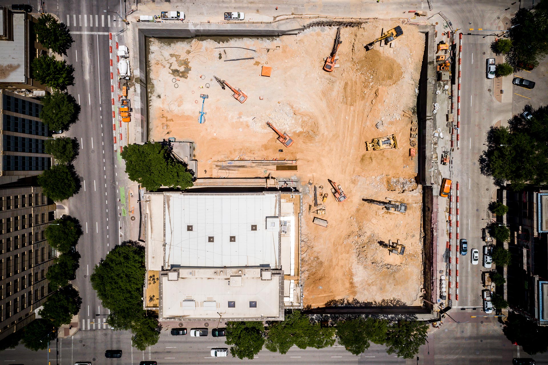 Aerial view of a major urban excavation site featuring Oscar Orduno, Inc. orange crawler excavators and engineered earth retention systems.